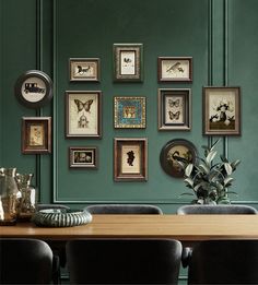 a dining room with green walls and framed pictures on the wall, along with black chairs