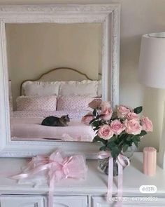 a white dresser topped with a mirror and pink flowers