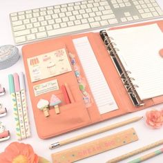 an open planner book sitting on top of a desk next to a keyboard and flowers