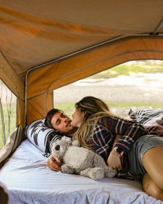 a man and woman laying in a tent with a teddy bear next to each other