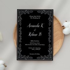 a black and white wedding card on top of a wooden plate next to cotton flowers