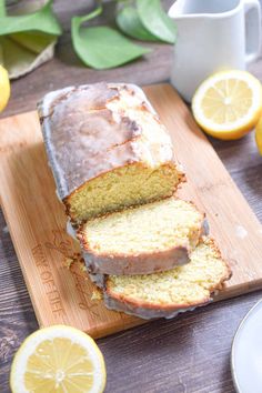 a loaf of lemon bread sitting on top of a wooden cutting board next to sliced lemons