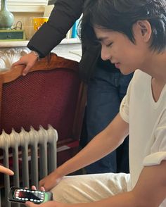 a young man sitting on the floor looking at his cell phone next to a radiator