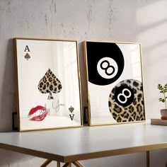 two framed art pieces sitting on top of a white table next to a potted plant