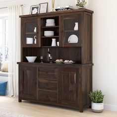 a dining room hutch with plates and bowls on the top shelf next to a potted plant