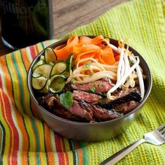 a bowl filled with meat and vegetables on top of a table next to a fork