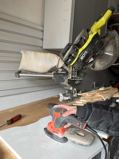 a man working on a piece of wood with a power tool in his hand and some other tools sitting next to him