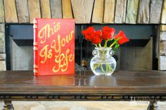 there is a vase with red roses in it next to a book on a table