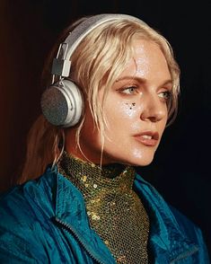 a blonde woman with headphones on her ears looking at the camera while standing in front of a dark background