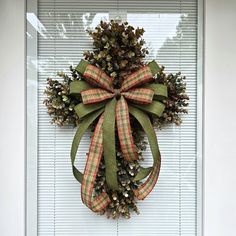 a christmas wreath hanging on the side of a door with green ribbon and pine cones