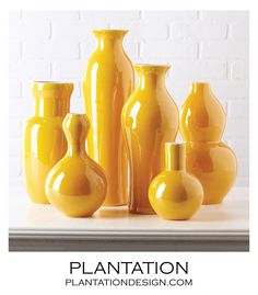 a group of yellow vases sitting on top of a white table next to each other