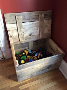 a wooden box filled with legos on top of a hard wood floor next to a red wall