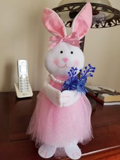 a stuffed rabbit in a pink tutu holding a blue flower and a remote control