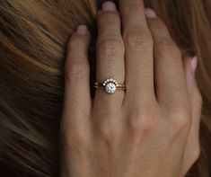 a woman's hand with a diamond ring on her left hand and brown hair in the background