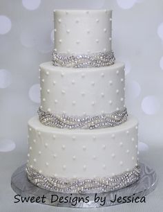 a three tiered cake with white frosting and silver decorations on the bottom layer