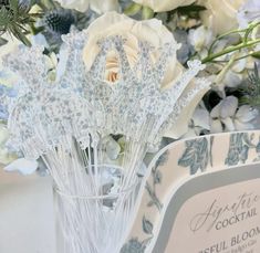 a vase filled with white and blue flowers next to a sign that says agent cocktail