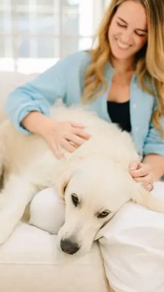 a woman sitting on a couch petting a white dog