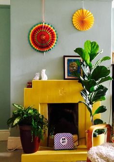 a living room with a yellow fireplace and potted plants on the mantel in front of it