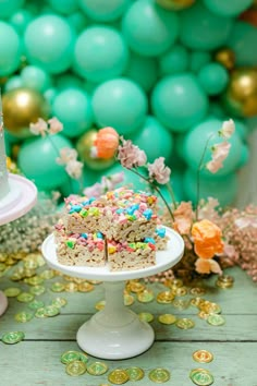 a birthday cake with sprinkles on it sitting in front of balloons and confetti