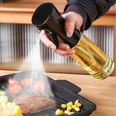 a person is pouring oil on a steak in a grill pan with vegetables and corn