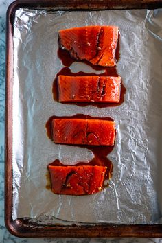 three pieces of cooked salmon sitting on top of aluminum foil covered in sauce and seasoning