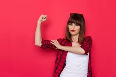 a woman posing with her arms up in front of a pink wall and wearing sunglasses