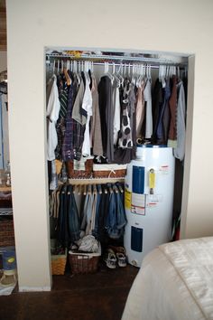 an open closet with clothes hanging on the rails, and a water heater nearby