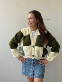 a woman standing in front of a white wall wearing a green and beige cardigan