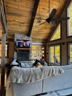 two people sitting on a couch in a living room with a fireplace and ceiling fan