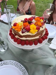 two women sitting at a table with a large cake on top of it, and one woman holding a glass of wine in the background