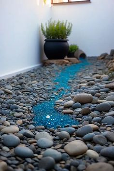 there is a blue stream running through the rocks on the ground next to a potted plant