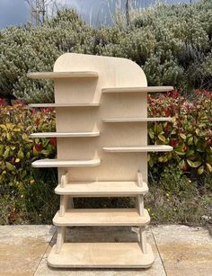 a wooden shelf sitting on top of a sidewalk next to bushes and shrubbery in the background