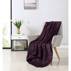 a chair with a purple blanket on top of it next to a table and flowers