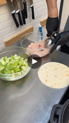 a person in black gloves preparing food on top of a counter with a bowl of lettuce and a tortilla