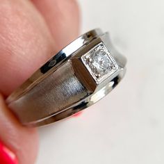 a close up of a person's hand holding a ring with a diamond on it