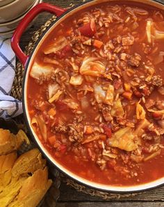 a large pot filled with meat and vegetables next to bread on a wooden table top