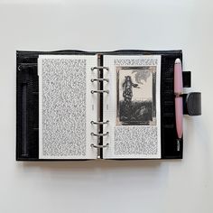 an open book on a white surface with a pen sticking out of the cover and writing