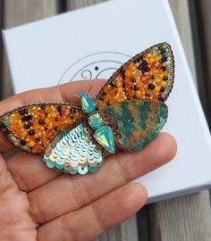 a hand holding a colorful butterfly brooch on it's finger, with the wings spread out