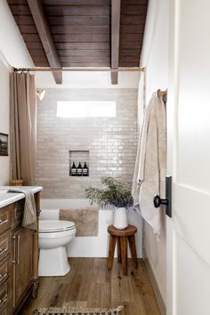 a white toilet sitting in a bathroom next to a wooden cabinet and counter with a potted plant on it