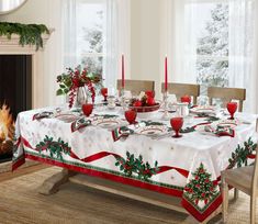 a dining room table set for christmas with red candles and holly wreaths on it