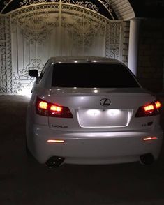 a white car is parked in front of a gate at night with its lights on