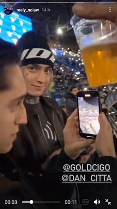 two men holding up cell phones in front of a beer glass at a sporting event