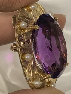 This gorgeous oval 36ctw amethyst is set in a 14kt yellow gold handmade engraved frame adorned with 8 cultured pearls that each measure 2.5mm. It can be worn as a brooch (pin) or a pendant. The amethyst measures 27mmx20mmx12mm, and the entire piece is 38mmx30mm and weighs 10dwt. Handmade in the 1960's it is a true vintage statement piece. It is truly a timeless work of art. Formal Amethyst Oval Cabochon Jewelry, Formal Amethyst Jewelry, Oval Cabochon, Elegant Yellow Gold Cabochon Amethyst Ring, Elegant Yellow Gold Amethyst Cabochon Ring, Exquisite Oval Brooch Jewelry, Elegant Gold Amethyst Cabochon Ring, Elegant Oval Cabochon Amethyst Ring For Formal Occasions, Formal Heirloom Amethyst Cabochon Ring, Formal Purple Oval Cabochon Jewelry