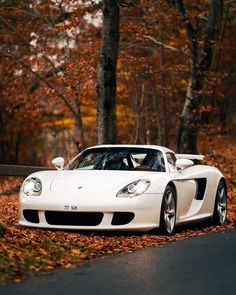 a white sports car parked on the side of a road in front of some trees