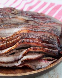 sliced bacon sitting on top of a wooden plate next to a red and white towel