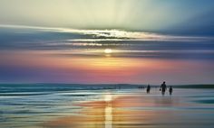 three people walking on the beach at sunset