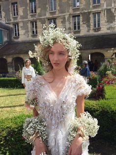 a woman in a white dress with flowers on her head is posing for the camera