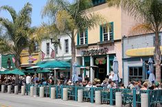 many people are sitting at tables in front of shops and palm trees on the sidewalk