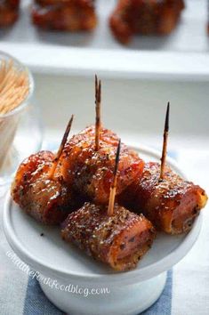 several skewered meats are sitting on a white plate with toothpicks