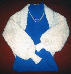 a blue shirt and white cardigan with pearls on the collar is sitting next to a necklace